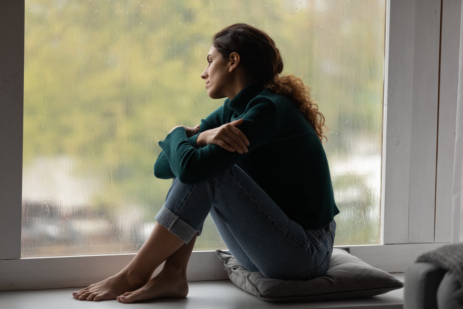 Woman sitting alone by a window looking thoughtful