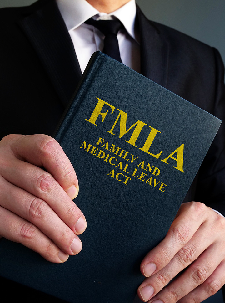 A person in a suit holds a book titled “FMLA Family and Medical Leave Act” with gold lettering on the cover.
