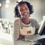 Smiling restaurant server in an apron standing at the register